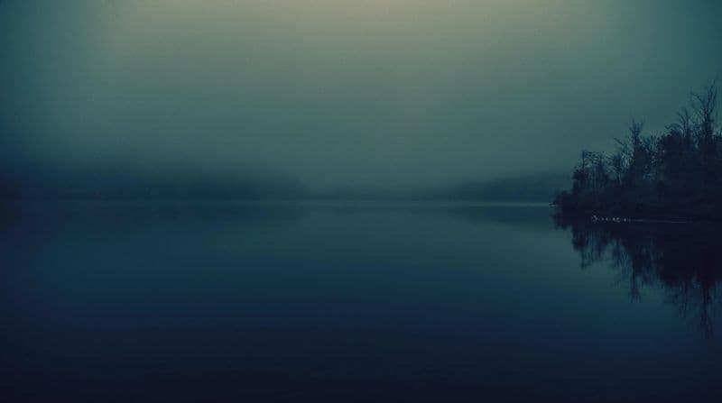 A still lake beneath a misty sky